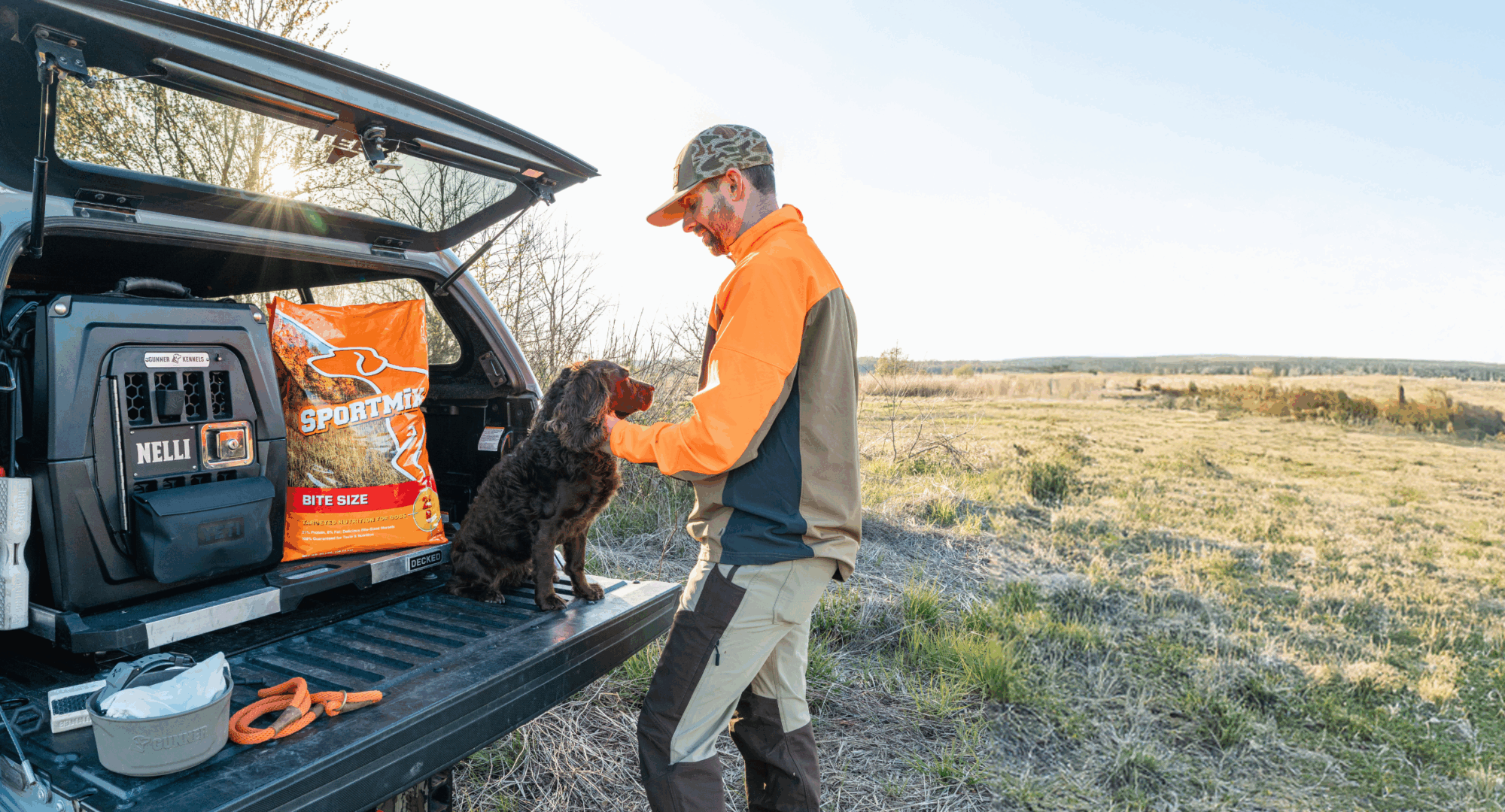 man pets dog as it sits on truck bed next to food